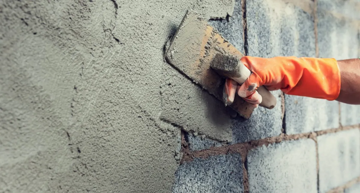 Plasterer working a backing coat onto blockwork