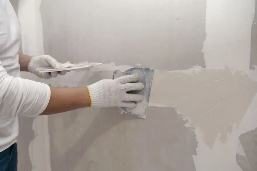 Plasterer applying plaster over plasterboard joints on a wall